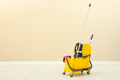 Photo of Mop bucket with cleaning supplies on floor near light wall