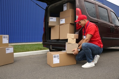 Photo of Courier loading packages in car trunk outdoors