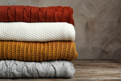 Photo of Stack of warm clothes on wooden table against grey background. Autumn season