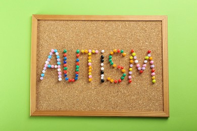 Corkboard with word Autism made of colorful pins on light green background, top view