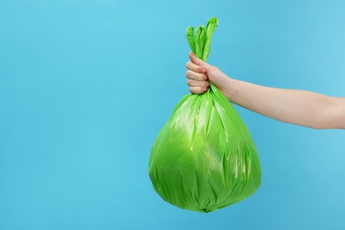 Photo of Woman holding plastic bag full of garbage on light blue background, closeup. Space for text