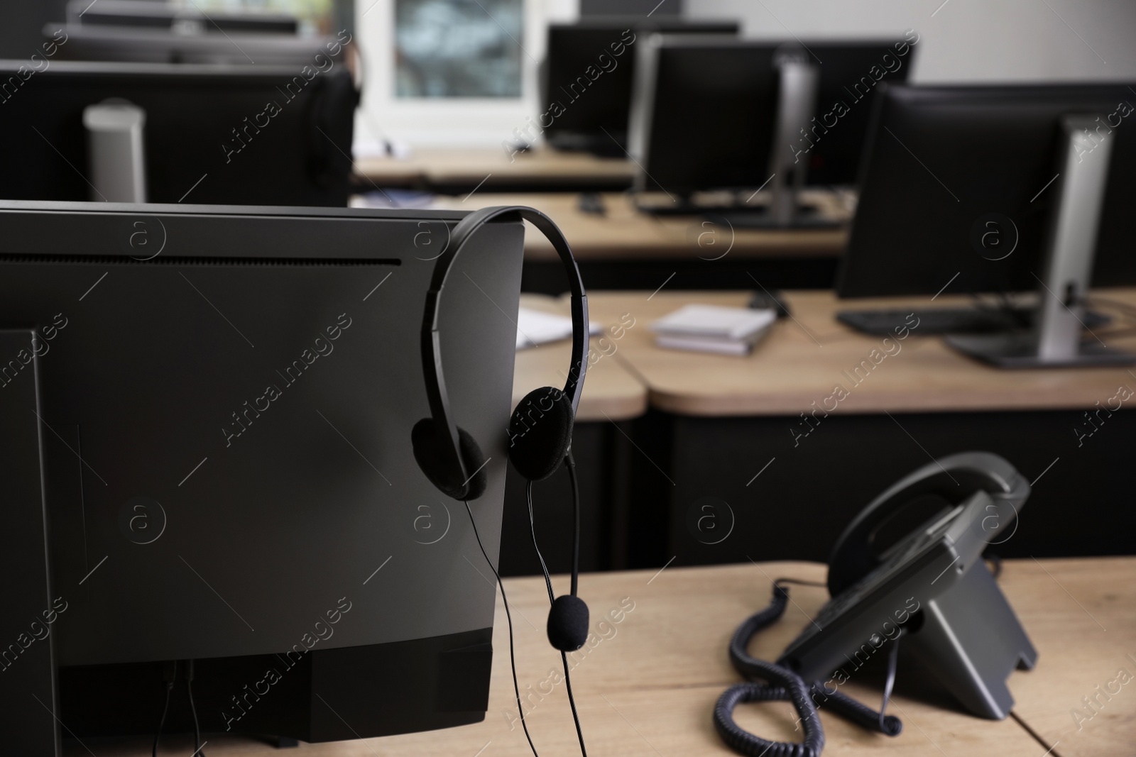 Photo of Stationary phone near modern computer with headset on wooden desk indoors. Hotline service