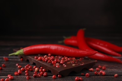Delicious chocolate, fresh chili pepper and red peppercorns on wooden table, closeup