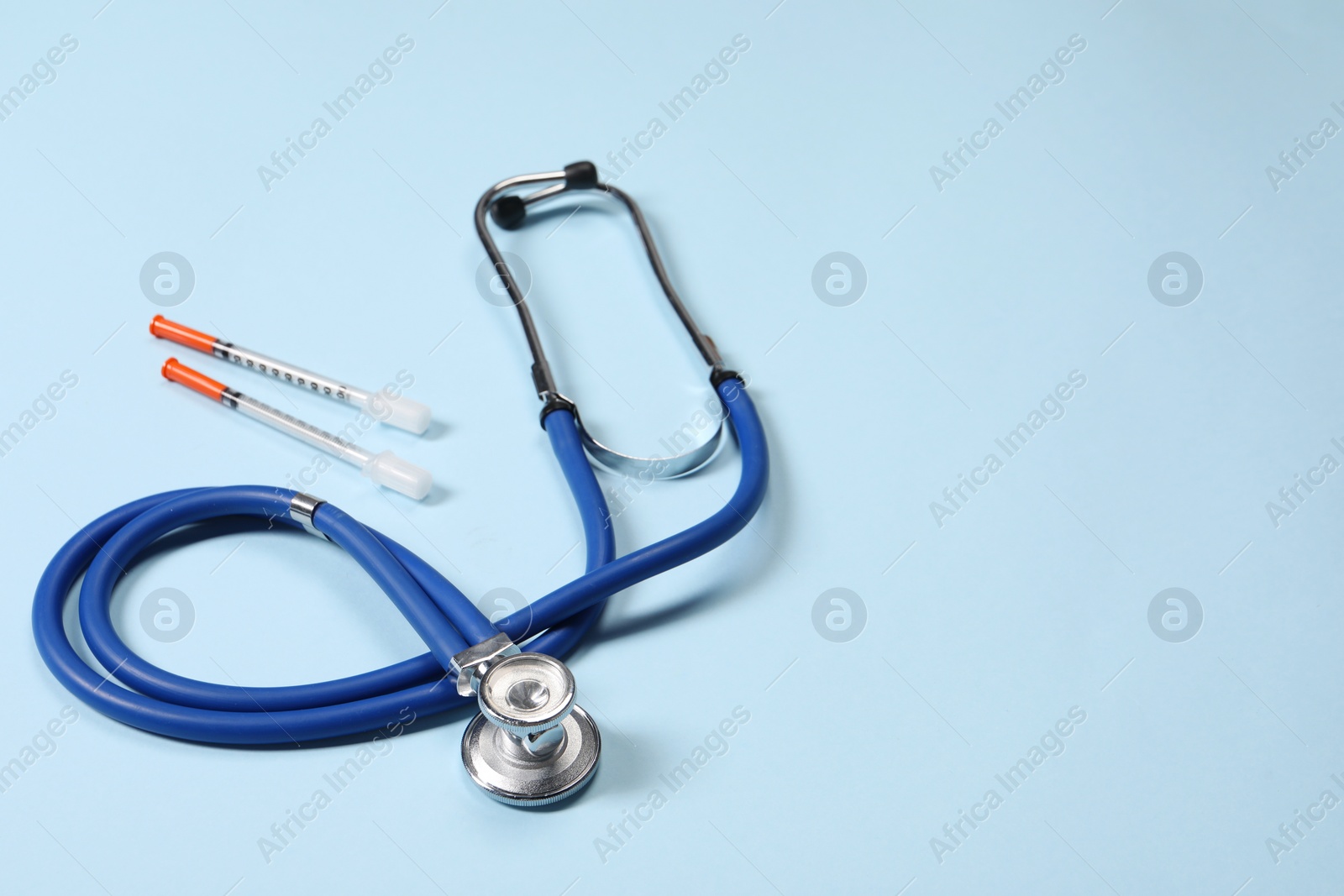 Photo of Stethoscope and syringes on light blue background. Space for text