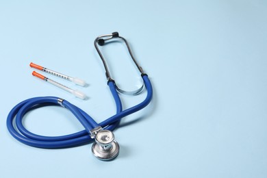 Stethoscope and syringes on light blue background. Space for text