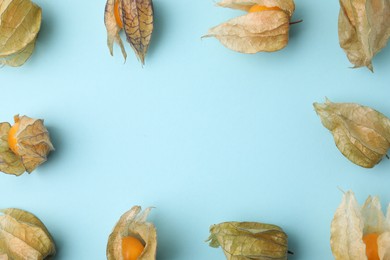 Photo of Frame of ripe physalis fruits with calyxes on light blue background, flat lay. Space for text