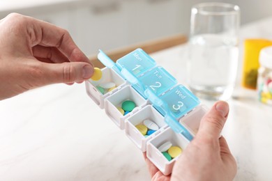 Woman with pills, organizer and glass of water at white marble table, closeup