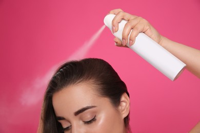 Young woman applying dry shampoo against pink background, closeup