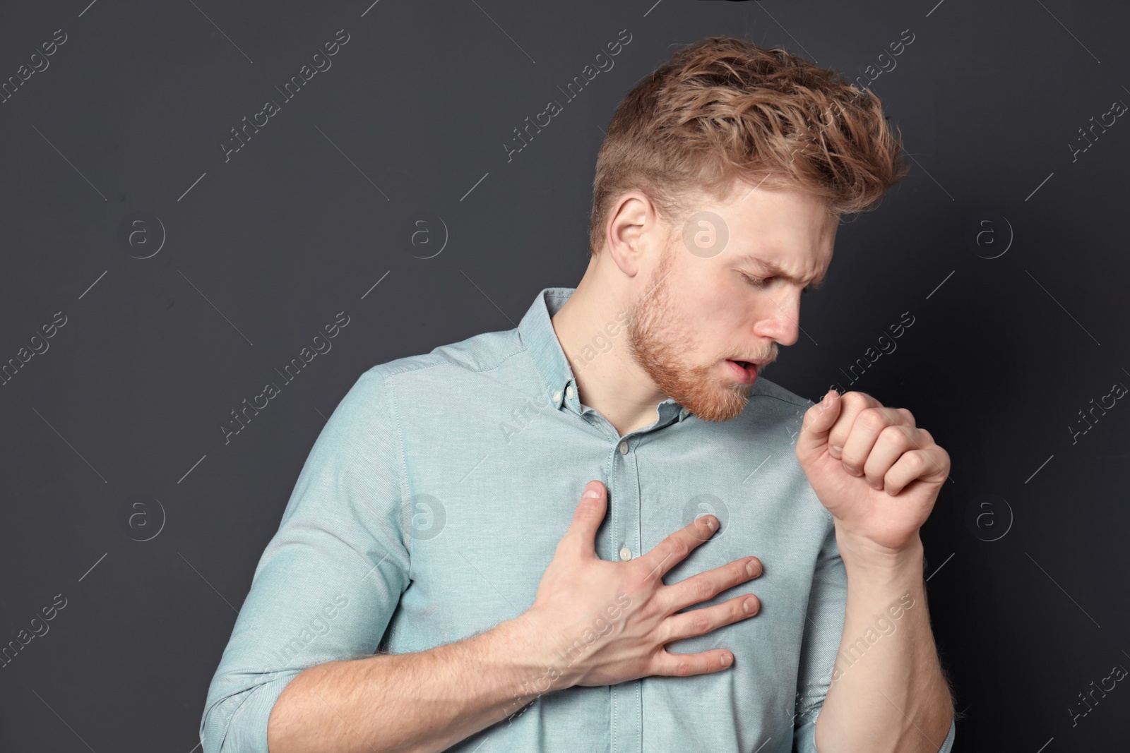 Photo of Handsome young man coughing against dark background