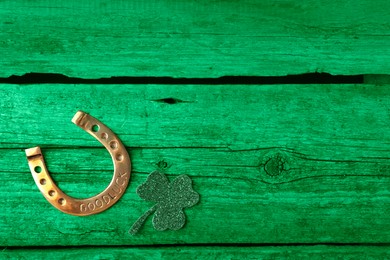 Image of St. Patrick's day. Decorative clover leaf and golden horseshoe on green wooden background, flat lay. Space for text