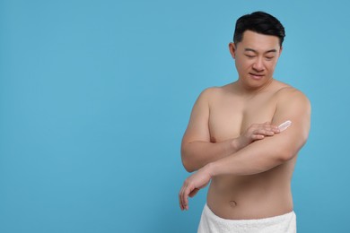 Photo of Handsome man applying body cream onto his arm on light blue background. Space for text