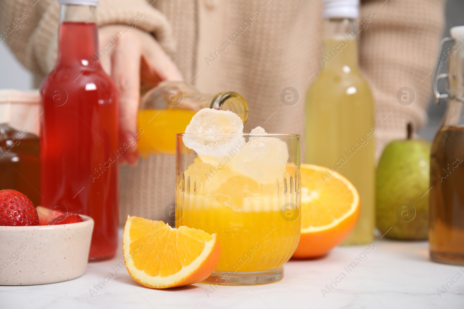 Photo of Woman pouring tasty kombucha into glass with ice at white table, closeup