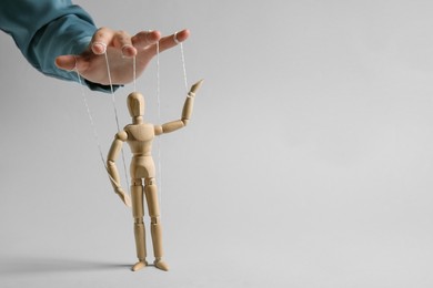 Photo of Woman pulling strings of puppet on light grey background, closeup. Space for text