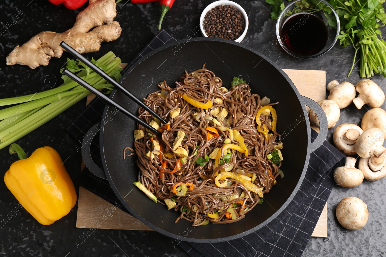 Photo of Stir-fry. Tasty noodles with meat and vegetables in wok served on dark textured table, flat lay