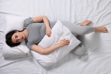 Young woman with pillow suffering from insomnia on bed, top view