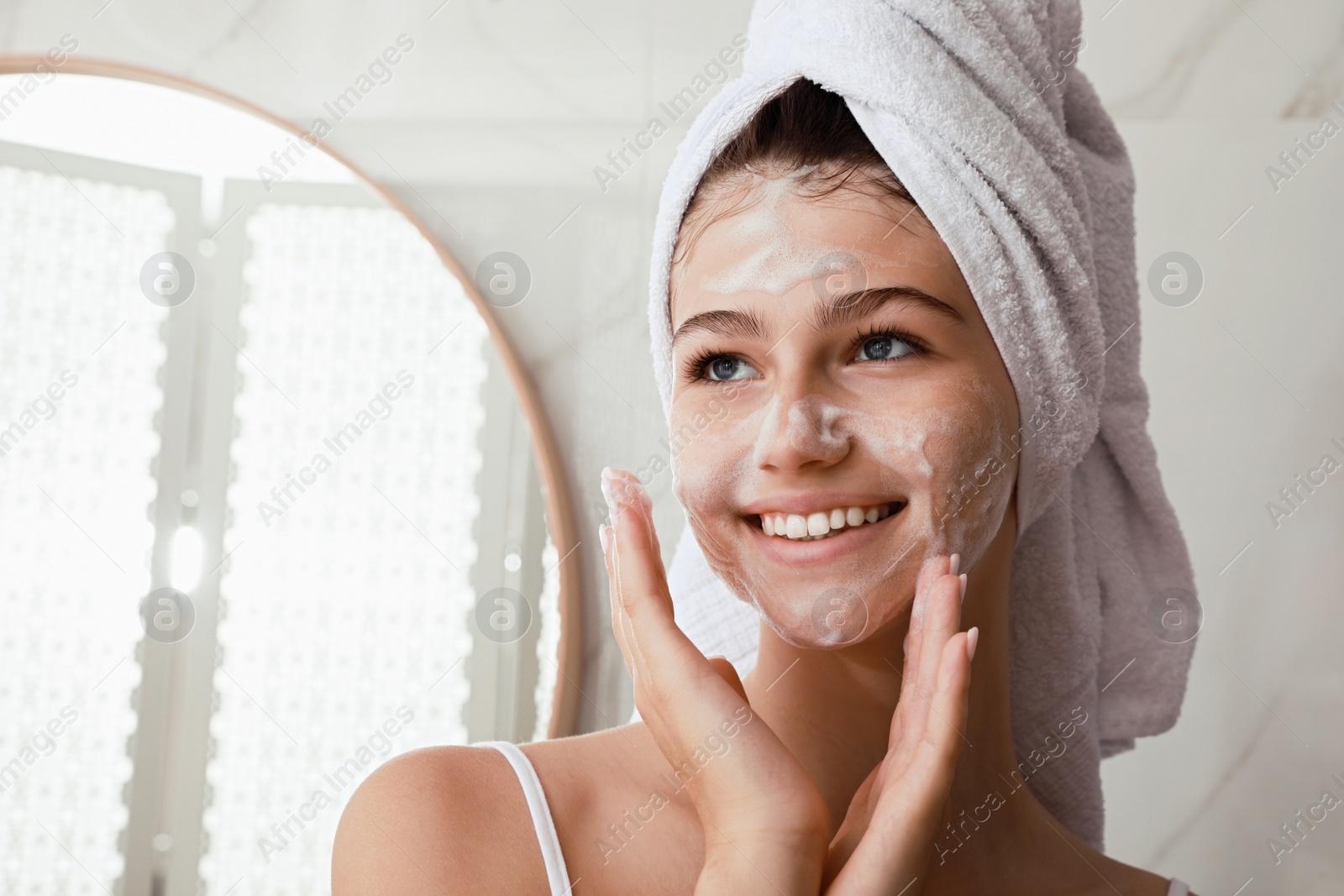 Photo of Beautiful teenage girl applying cleansing foam onto face in bathroom, space for text. Skin care cosmetic