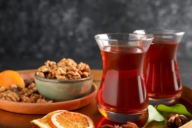 Photo of Tray with glasses of traditional Turkish tea, walnuts, dried orange and anise on table, closeup
