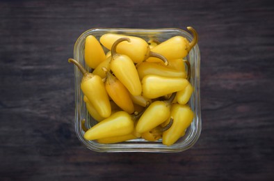 Photo of Bowl of pickled yellow jalapeno peppers on wooden table, top view