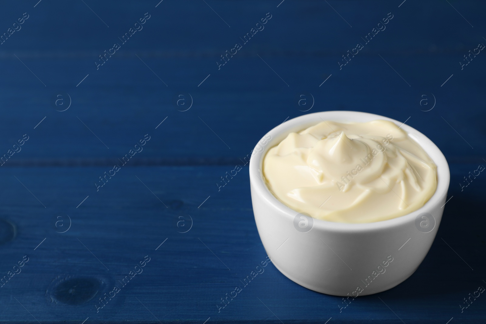 Photo of Tasty mayonnaise in bowl on blue wooden table, closeup. Space for text