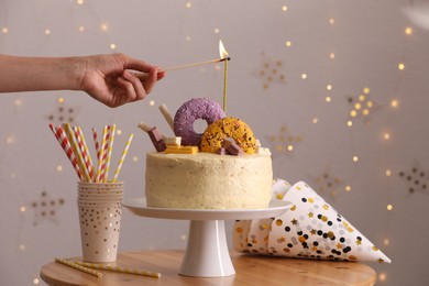 Woman lighting candle on delicious cake decorated with sweets at wooden table, closeup