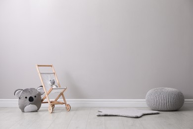 Toy stroller with bear and pouf near grey wall in child room. Interior design
