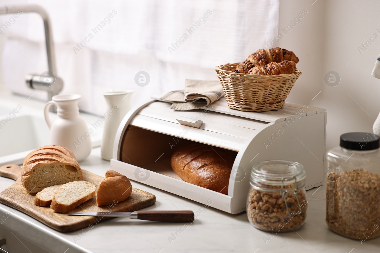 Photo of Wooden bread basket with freshly baked loaves on white marble table in kitchen