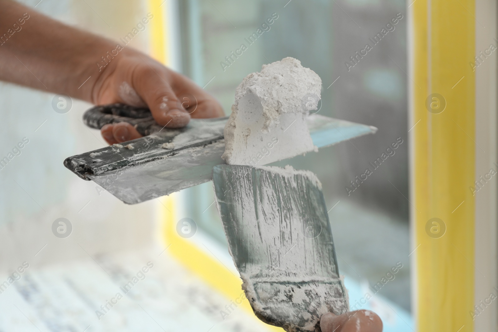 Photo of Professional worker with putty knifes and plaster near window indoors, closeup. Interior repair