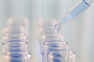 Photo of Laboratory analysis. Dripping light blue liquid from pipette into glass test tube on blurred background, closeup