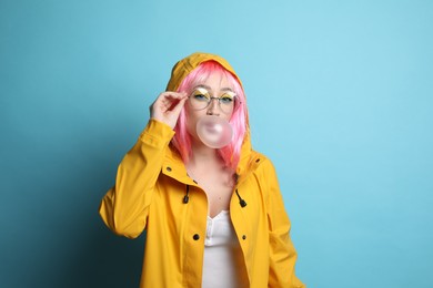 Photo of Fashionable young woman in pink wig with bright makeup blowing bubblegum on yellow background