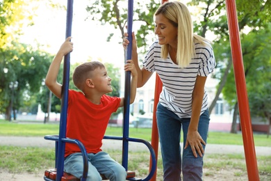 Nanny and cute little boy on swing in park