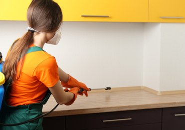 Pest control worker spraying pesticide in kitchen