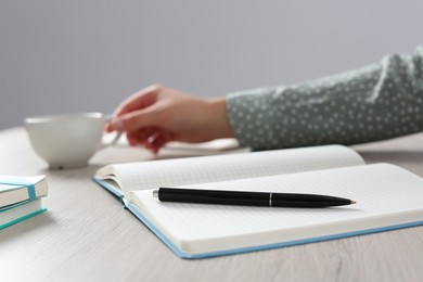 Photo of Woman with cup of drink at wooden table in office, focus on notebook and pen