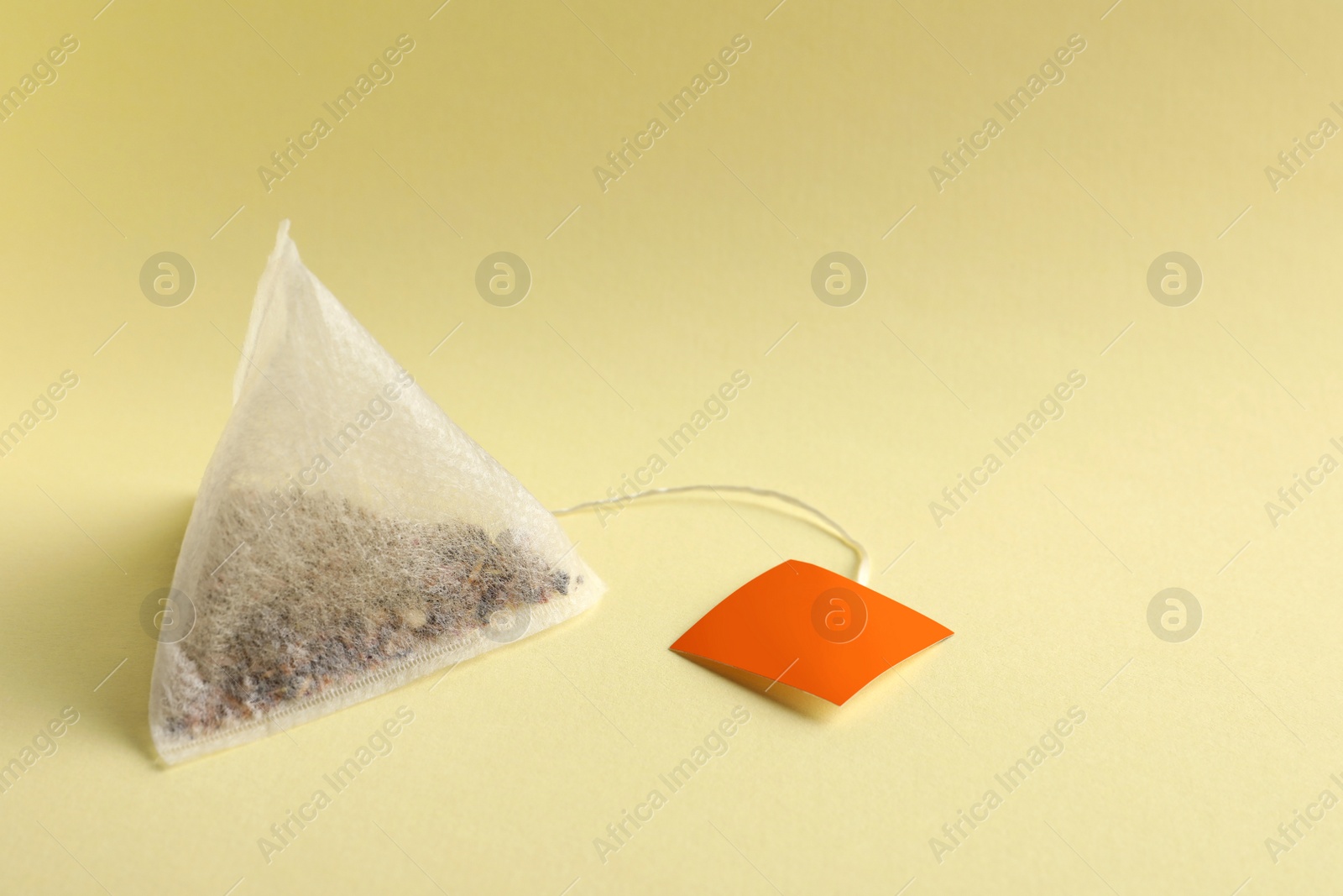 Photo of New tea bag with tab on yellow background, closeup. Space for text