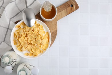 Photo of Breakfast cereal. Tasty corn flakes, milk, honey and spoon on white tiled table, top view. Space for text