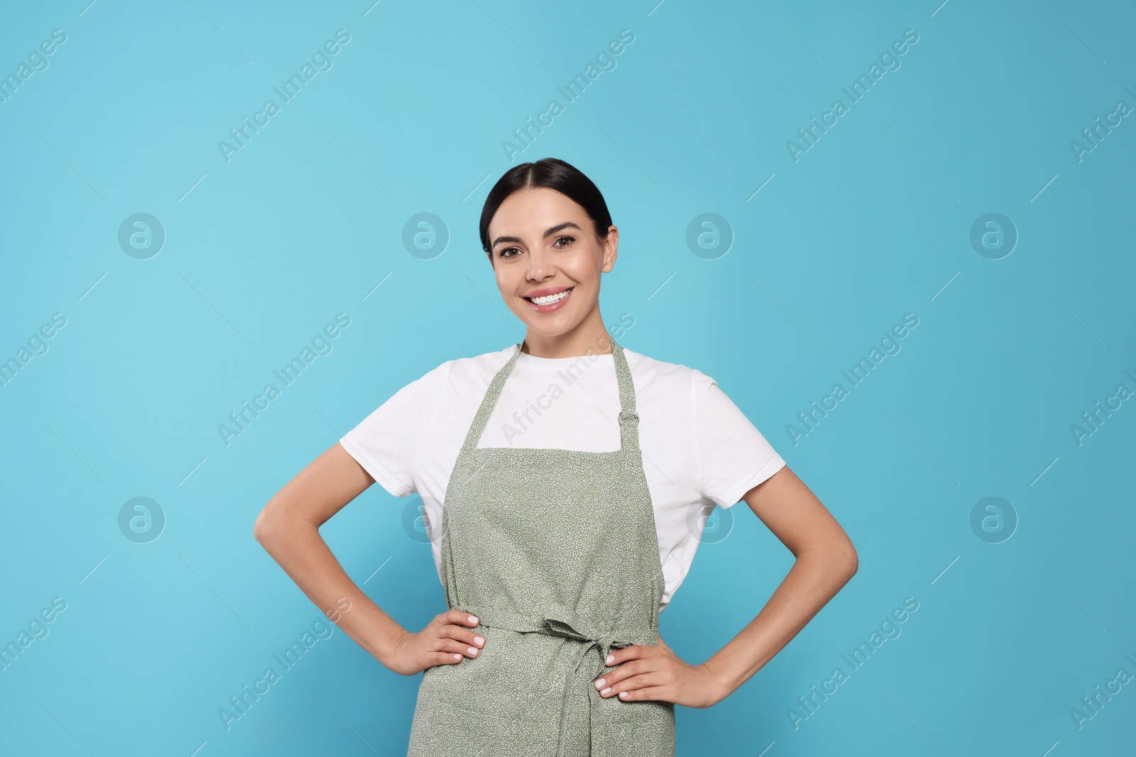 Photo of Young woman in grey apron on light blue background,