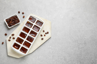 Photo of Ice cubes with coffee beans in tray on grey table, flat lay. Space for text