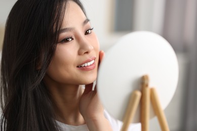 Woman with perfect skin looking at mirror indoors