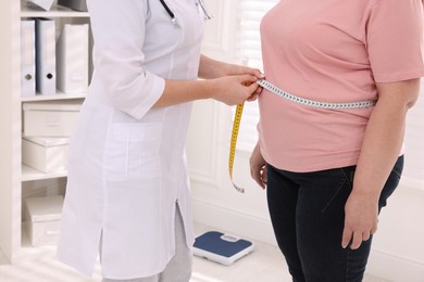 Photo of Nutritionist measuring overweight woman's waist with tape in clinic, closeup