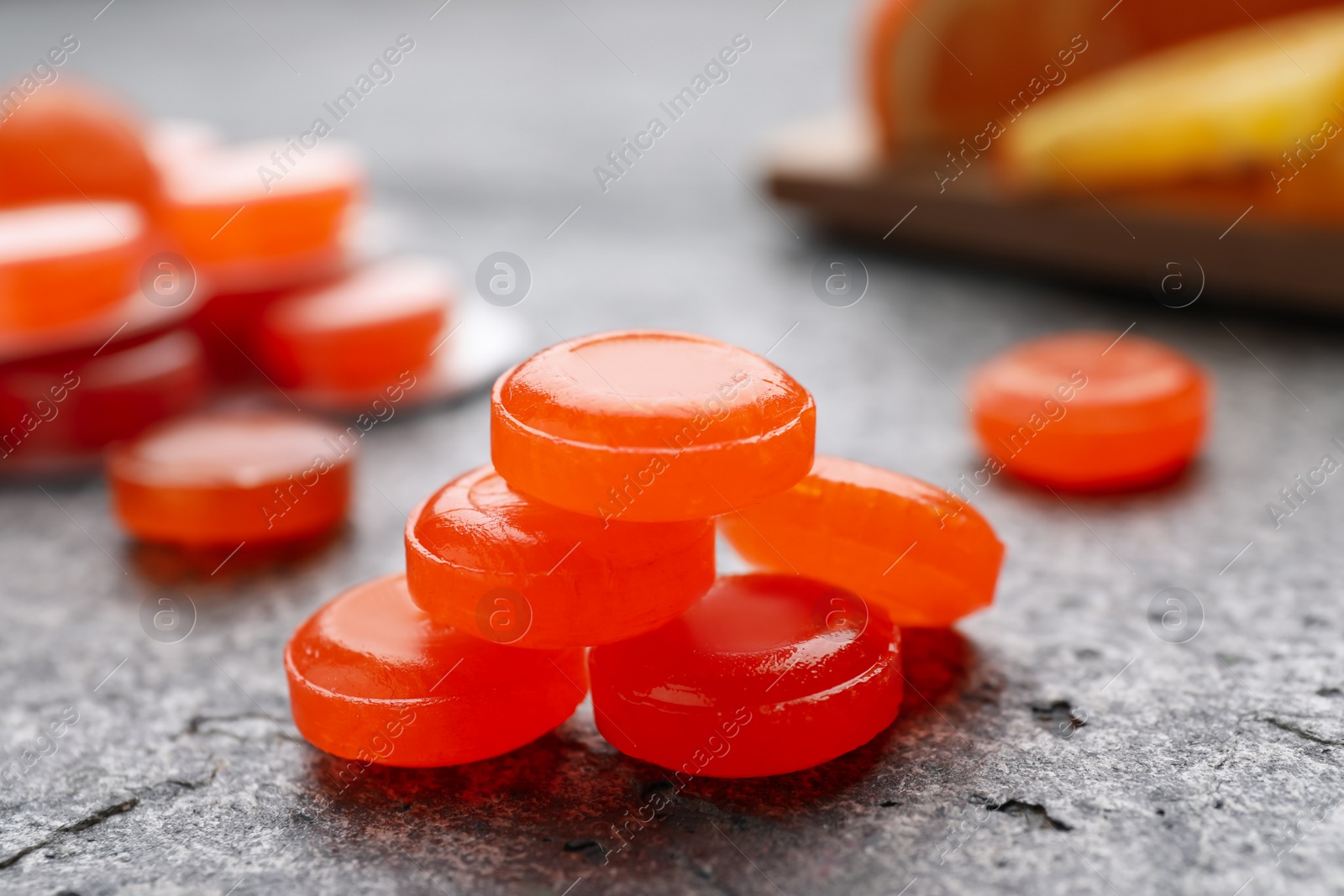 Photo of Many orange cough drops on grey table, closeup