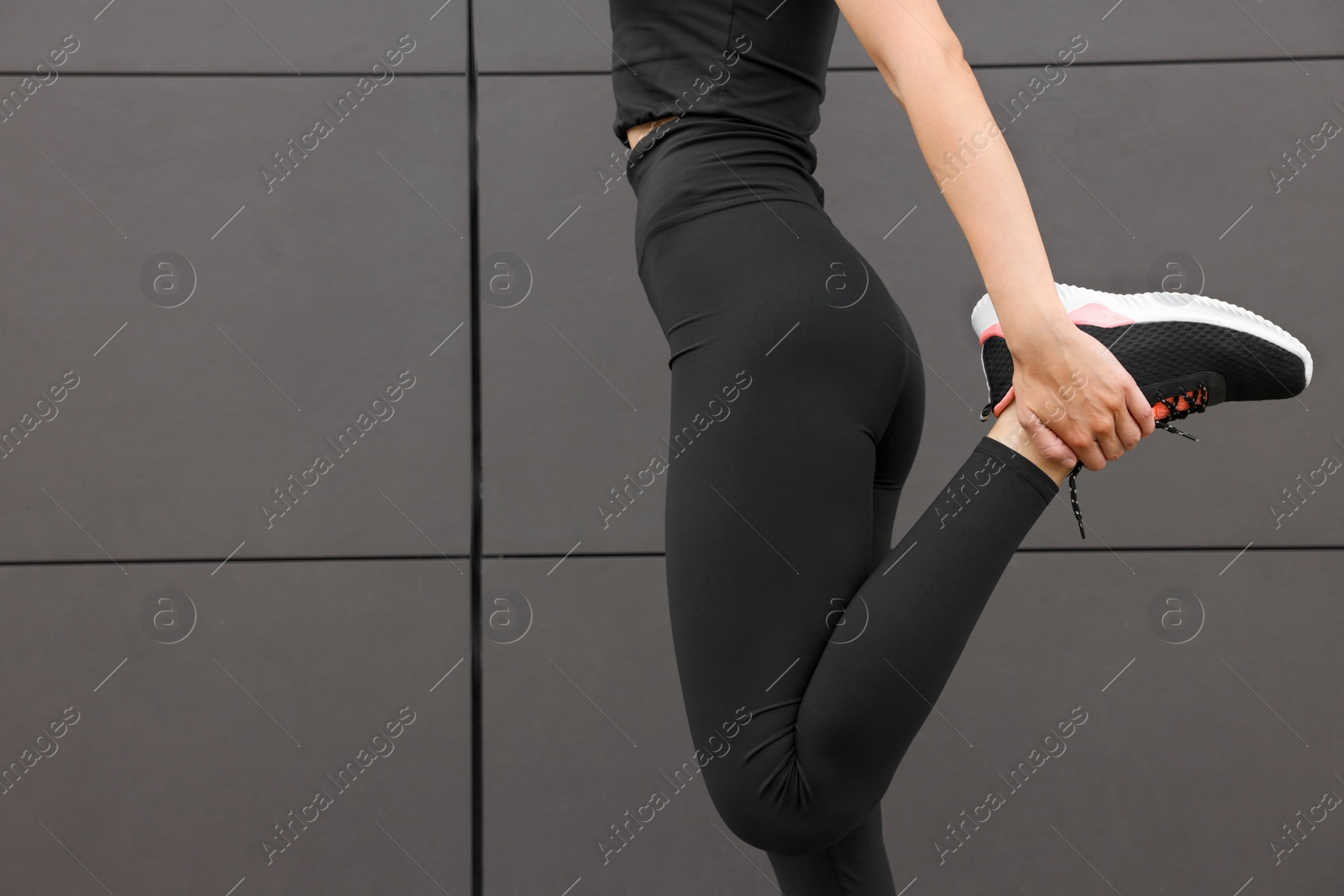 Photo of Woman in gym clothes doing exercises near grey wall on street, closeup. Space for text