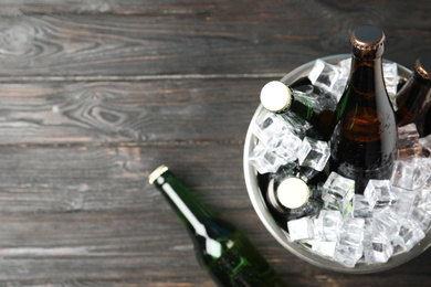 Photo of Metal bucket with bottles of beer and ice cubes on black wooden background, top view. Space for text