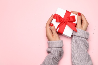 Young woman holding Christmas gift on pink background, top view. Space for text