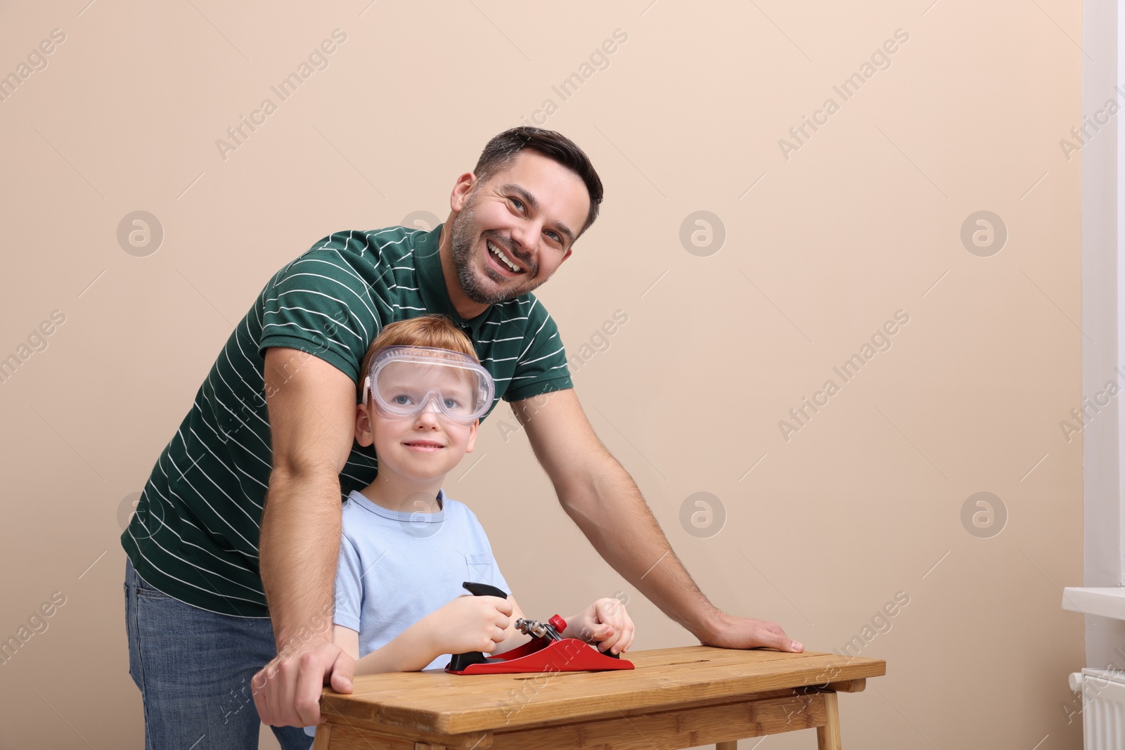 Photo of Father teaching son how to work with plane near beige wall
