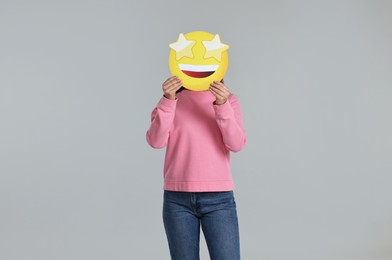 Photo of Woman holding emoticon with stars instead of eyes on grey background