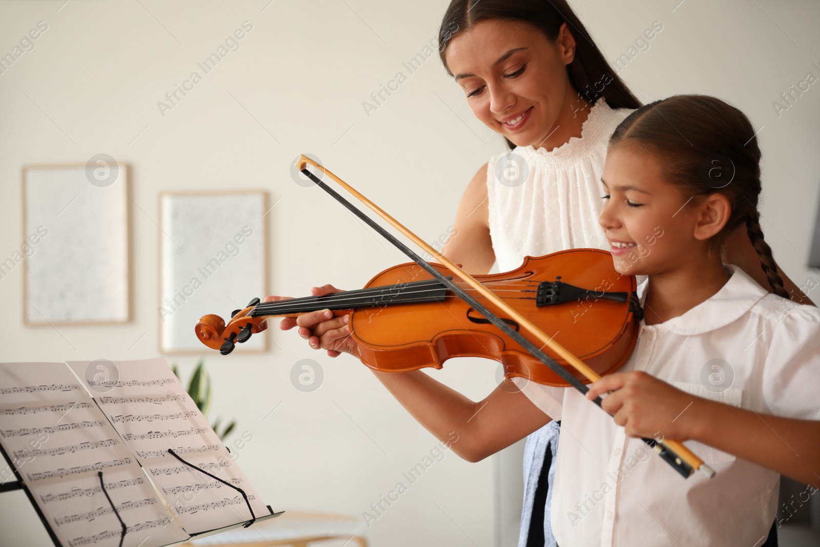 Photo of Young woman teaching little girl to play violin indoors