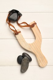 Slingshot with stones on white wooden background, flat lay