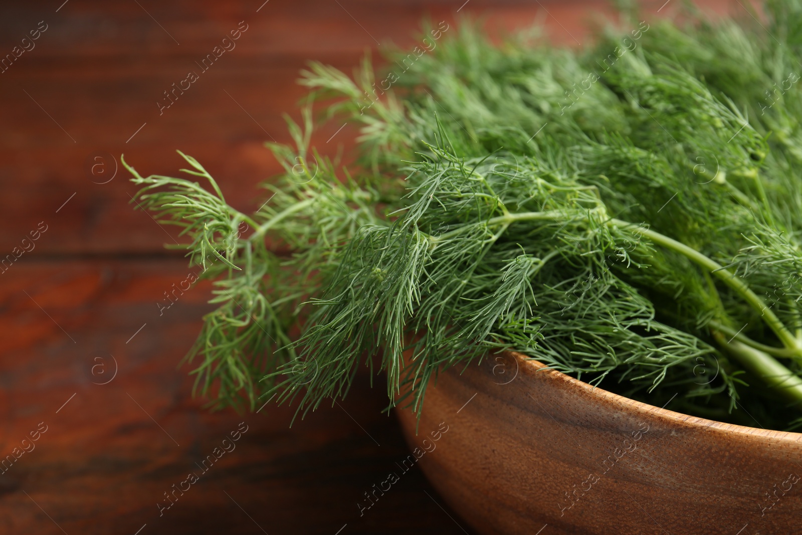 Photo of Bowl of fresh green dill on wooden table, closeup