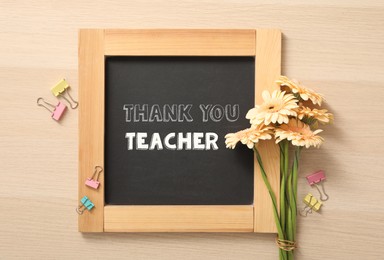 Image of Blackboard with phrase Thank You Teacher and flowers on wooden table, flat lay