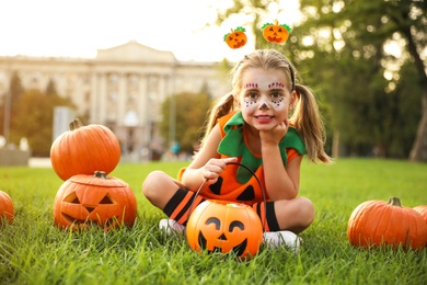 Photo of Cute little girl with pumpkin candy bucket wearing Halloween costume in park