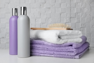 Photo of Folded towels, hair brush and shampoo on table against white wall.